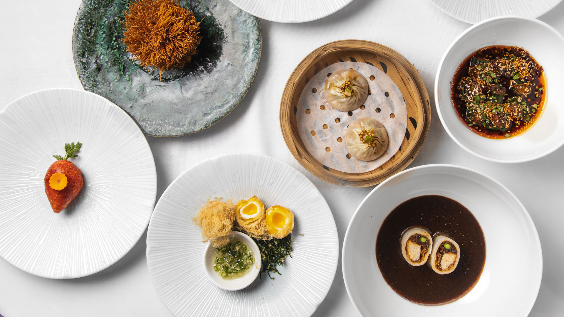 A bird's-eye photo of plates of Chinese dim sum from A.Wong on a table including dumplings and dishes with meat with sauce