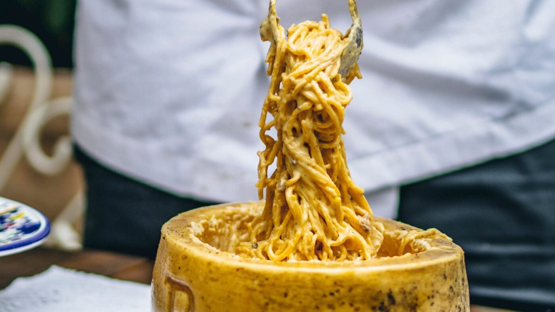 Fresh pasta being lifted from a wheel of cheese, coated in creamy sauce at a restaurant.