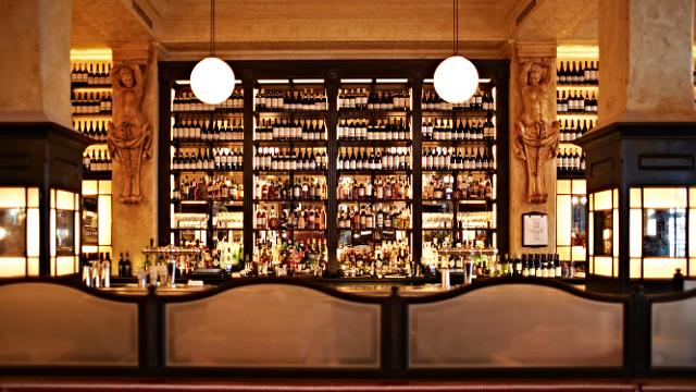 A yellow-lit bar with bottles lining the back wall at balthazar london.