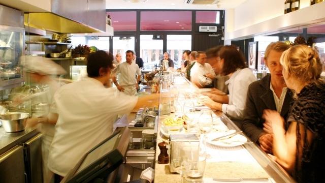 People sitting at the counter eating while servers move behind the counter.
