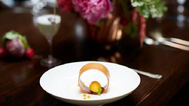 A white dessert dish on a black table with flowers and cocktails behind it at berners tavern london.