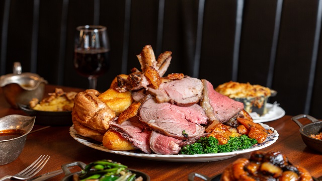 A plate piled high with roast meat, potatoes and vegetables, set on a wooden table with side dishes surrounding the plate