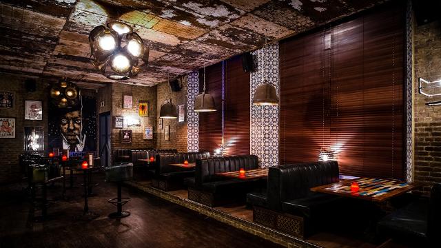 A dimly lit american-style bar in london with booths and lamps and high ceilings.