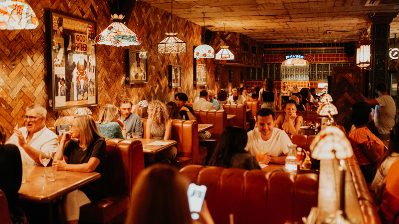 Enjoy delicious barbecue and live music at The Blues Kitchen. Credit: Josh Hiatt. Image courtesy of The Blues Kitchen. Diners sat in booths with exposed brick walls and yellow lighting