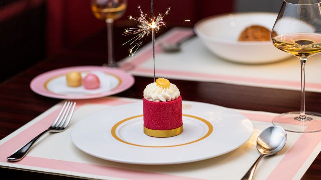 A pink place setting with a red dessert topped with cream and a sparkler at bob bob ricard restaurant in london.