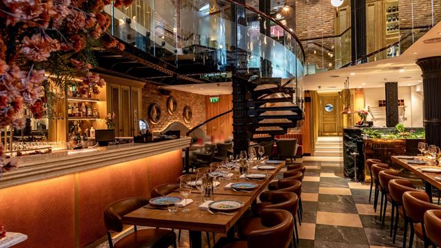 The interior of Bocconcino Mayfair, featuring tiled floors, a spiral staircase, floral displays and a long bar.