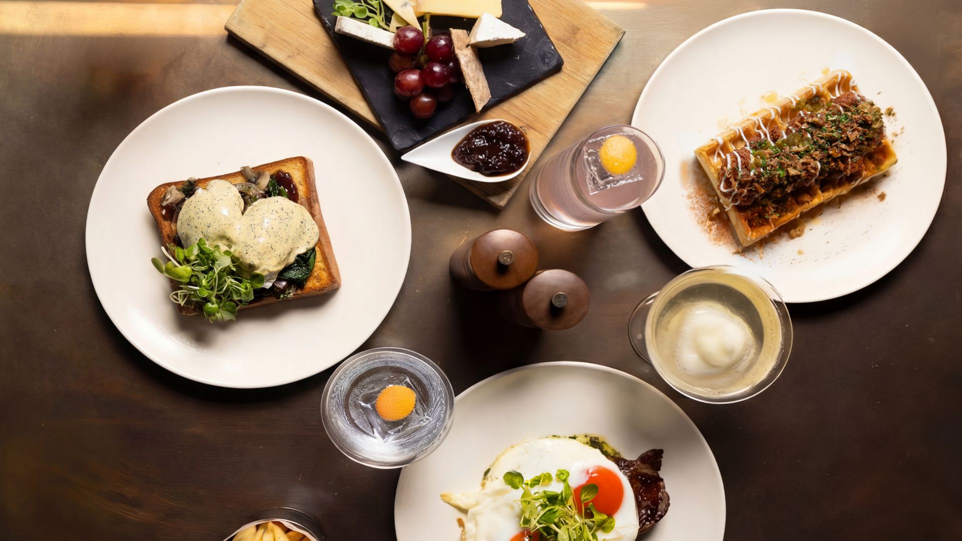 Overhead view of brunch dishes and cocktails on a table, including eggs, waffles and cheese.