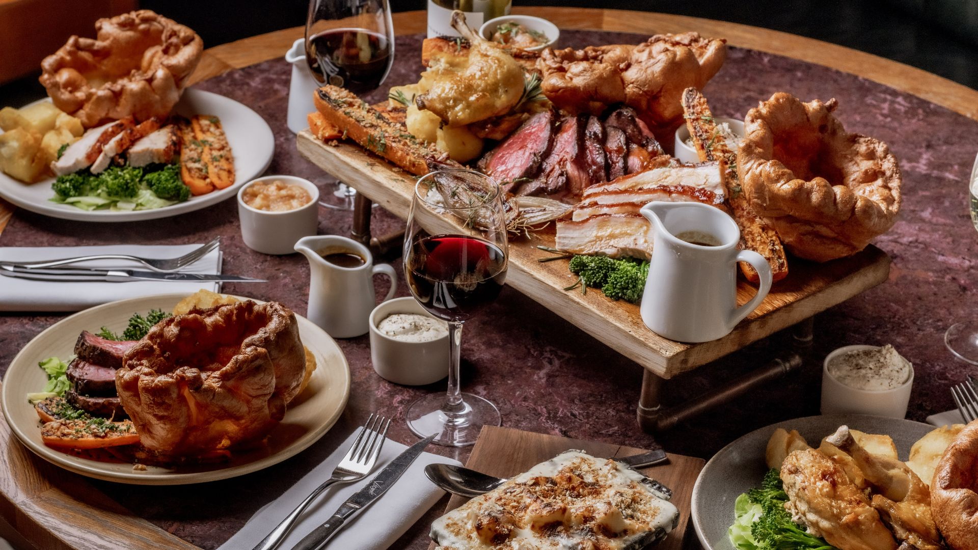 A large Sunday roast spread with Yorkshire puddings, roasted meats, vegetables and gravy served on a table.