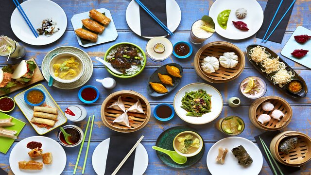 high angle shot of dozens of small to medium bowls with Chinese cuisine including dumplings, spring rolls and noodles
