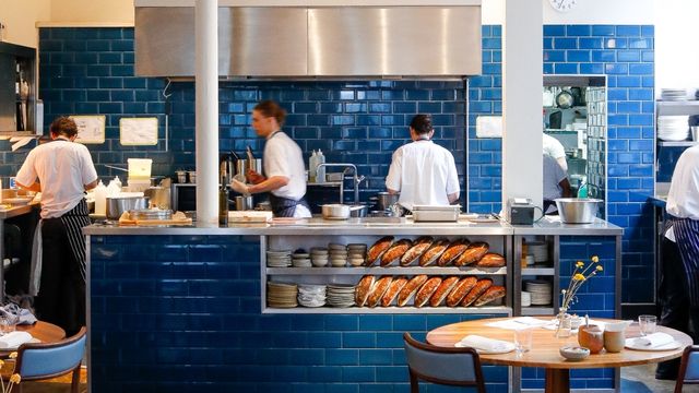 A blue counter with chefs working together and tables in front.