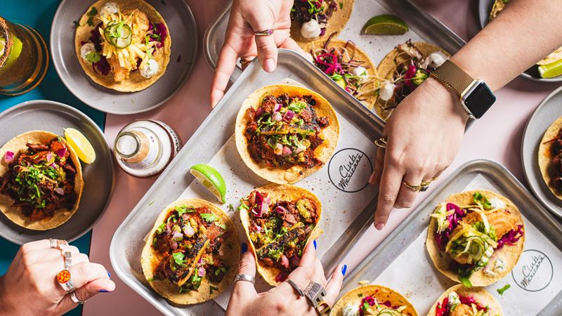 Mingle with mates over tacos and margaritas at Club Mexicana. Credit: Nic Crilly-Hargrave. Image courtesy of Club Mexicana. A birds-eye photo of Mexican tacos on a table with someone's hand holding one of them at Club Mexicana