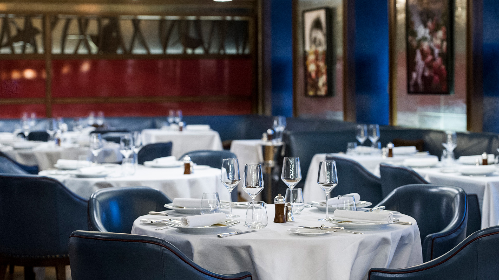 The empty dining room at Corrigan's Mayfair, with blue velvet chairs and white tablecloths.