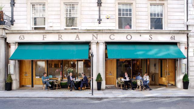 Landscape photo of the outside of Franco's - gold decor and green awnings outside the window