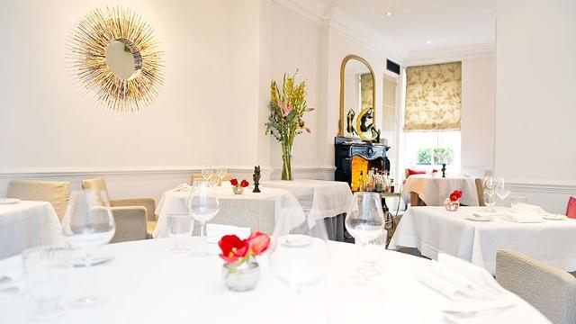 The elegant and brightly lit dining room at French restaurant, Gauthier Soho, complete with white tablecloth and white walls.