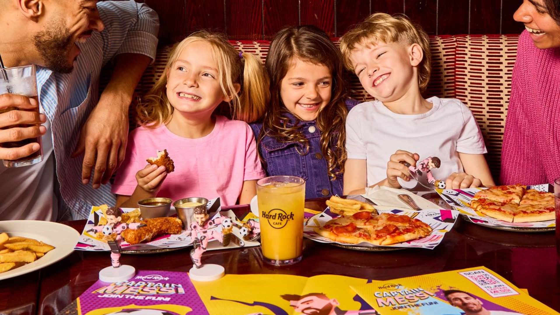 Family enjoying pizza, chicken and drinks together in a lively Hard Rock Cafe restaurant.