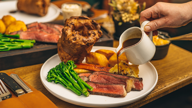 A table spread of roast dinners, with gravy being poured onto the plan in a small white jug