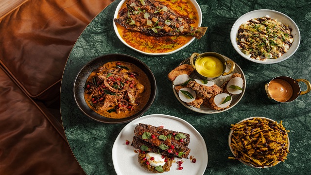 high angle shot of 5 white bowls varying in size with authentic Indian cuisine including curry, on a dark green round table
