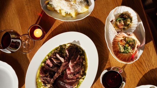 Aerial view of oval dishes on a wooden table, including pork, scallops and potatoes.