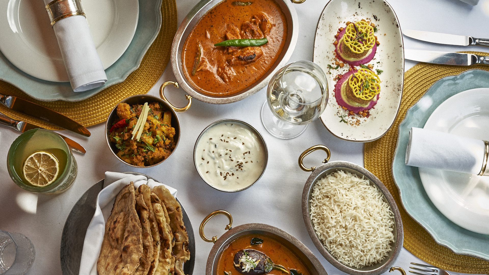 Indian dishes laid out on table with white tablecloth, including curry, rice, dips and naan bread.