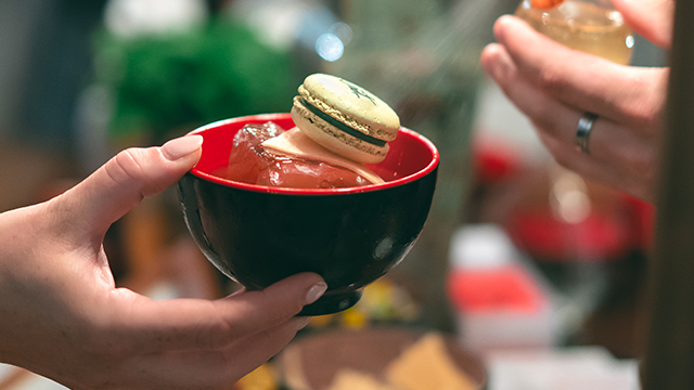 Opium Cocktail & Dim Sum Parlour. Image courtesy of The Breakfast Club. A hand holds a black and red Chinese rice bowl, filled with ice and a macaron.