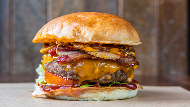 Close up on a beef burger topped with bacon and smokey cheese featured on the menu at Patty and Bun.