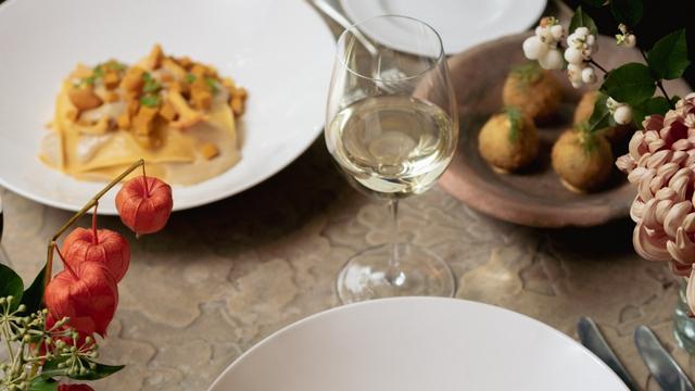 A table with white wine and a plate of pasta next to flowers at the petersham in covent garden