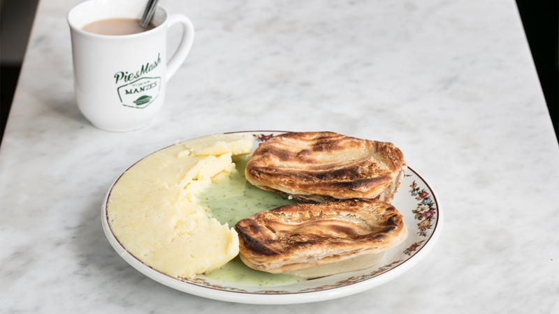 Tuck into delicious pie and mash from London's longest running pie shop. Credit: M.Manze. Image courtesy of M.Manze. A plate with two pies, mash and green liquor alongside a cup of tea
