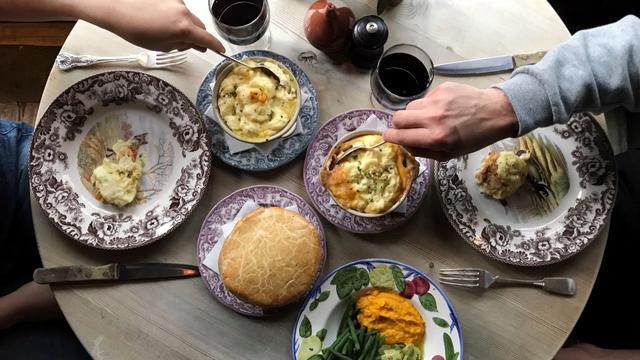 A table with plates covered in food as hands take spoonfuls of pie.
