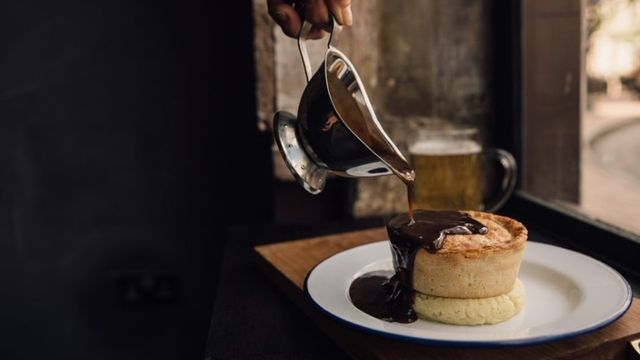 A white plate with a beige pie with brown gravy being poured over it.