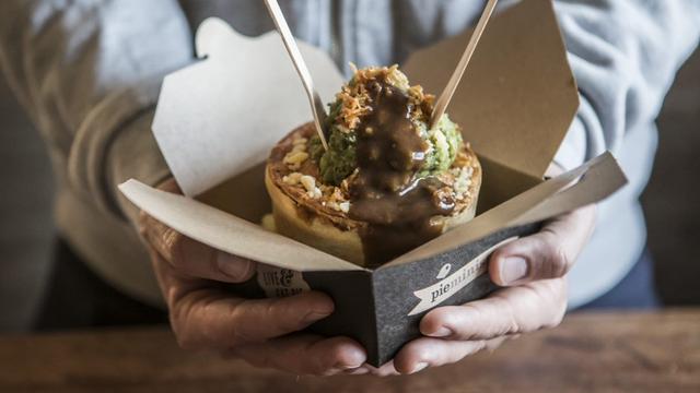 A hand holds a box with a pie covered in mushy peas and gravy from pieminster.