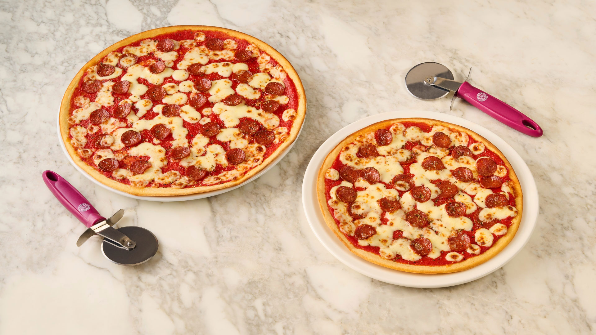 Choose from any toppings on Pizza Express' menu and swap to a gluten-free base. Image courtesy of Pizza Express. A photo of two gluten-free pizzas with cheese, tomato and pepperoni at Pizza Express with pizza cutters next to each