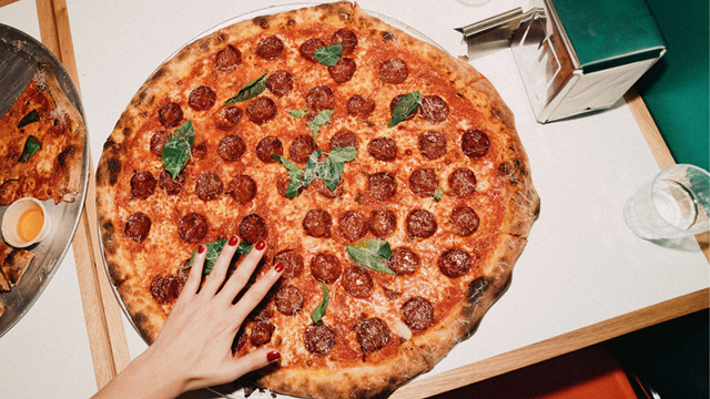 A 16-inch pepperoni pizza with a hand just above to indicate size comparison