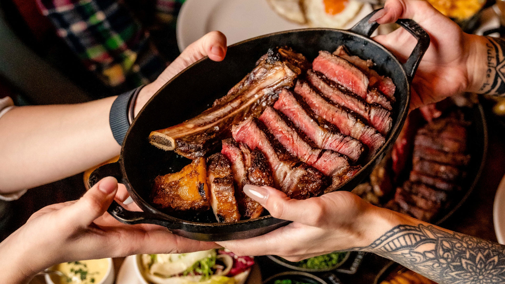 A bird's-eye photo of the sharing steak at Hawksmoor with a pair of hands passing the dish over to another pair of hands