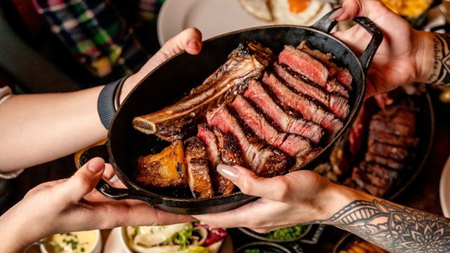 A bird's-eye photo of the sharing steak at Hawksmoor with a pair of hands passing the dish over to another pair of hands