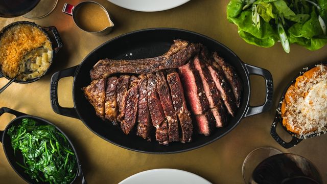 A table covered in food including a large pan with sliced steak in the centre with several potato and vegetable dishes beside it.