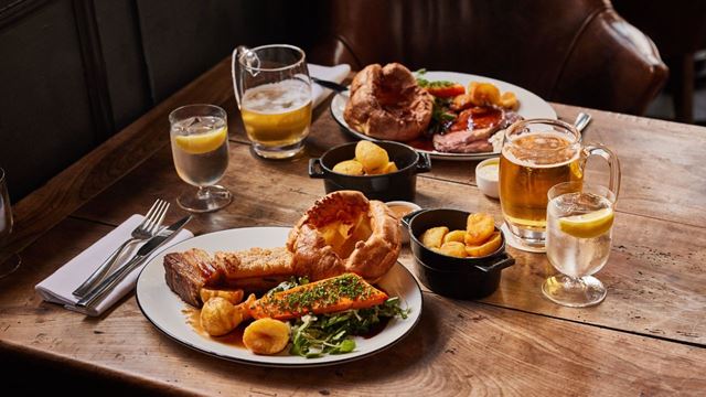 Deux assiettes sont disposées sur une table en bois et contenant des tranches de rôti, pommes de terres et Yorkshire Pudding.