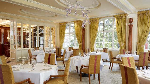 The elegant interiors of The Dining Room at The Goring, featuring yellow curtains and chairs and white tablecloths.