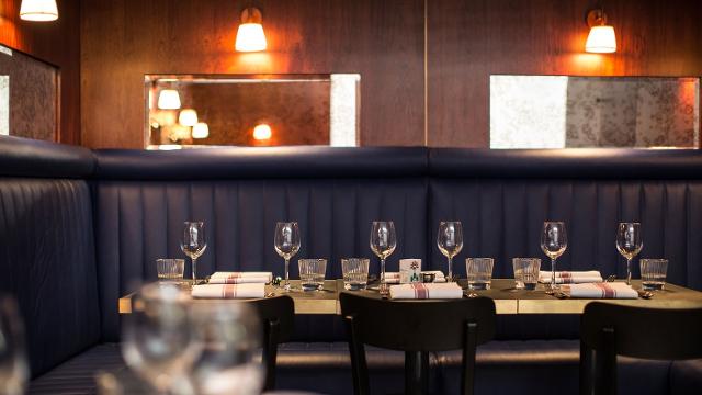 Dark blue banquette seating with dining table laid out with wine glasses, napkins and cutlery inside The Palomar restaurant in London's Soho.