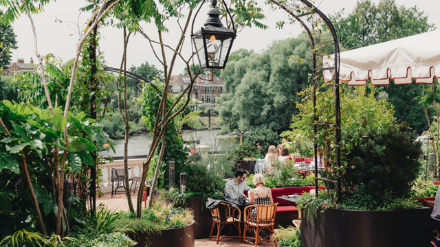 Outdoor dining terrace at Tower House restaurant surrounded by plants overlooking the river Thames.