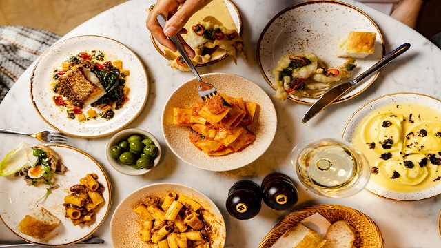 Birdseye shot of small plates of Italian pasta and side dishes with a person tucking into one of the plates