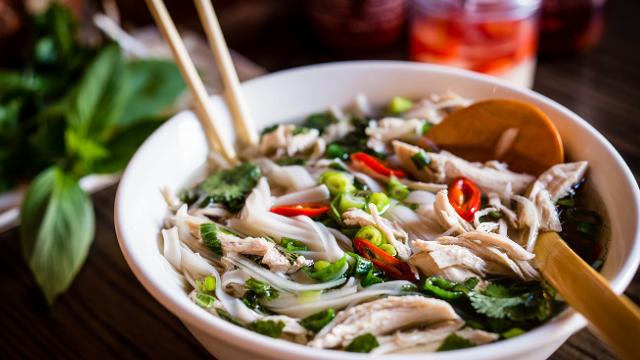 Taste delicious noodle soups at London's best Vietnamese restaurants. Credit: Pho. Image courtesy of Pho. Bowl of Vietnamese chicken noodle soup known as pho, with green vegetables and red chili, chopsticks and a wooden spoon.