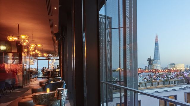 Ein Bild der Savage Garden Rooftop Bar in London, das die warmen orangefarbenen Innenräume und das offene Dach in der Nähe des Shard zeigt.