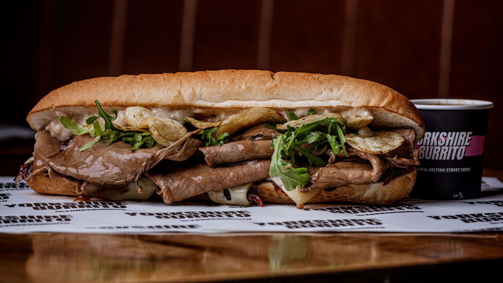 A photo of a yorkshire pudding burrito filled with slices of roast beef with a side of dipping gravy