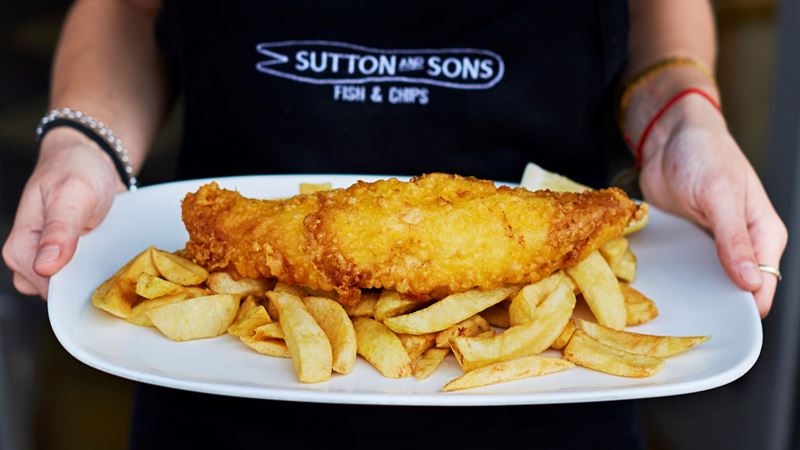 Opt from classic fish and chips or try something different on Sutton and Sons' changing menu. Credit: Sutton and Sons. Image courtesy of Sutton and Sons. A photo of a worker at Sutton and Sons holding a plate of battered fish on a bed of chips