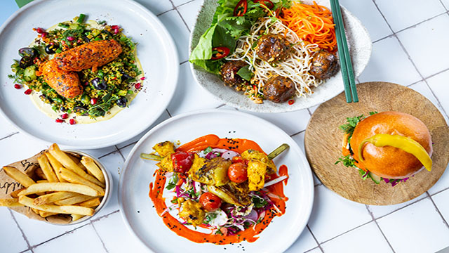 Une sélection de différents plats végétaliens tels que des hamburgers à base de plantes, des kebabs et des sautés, présentés dans des assiettes individuelles.