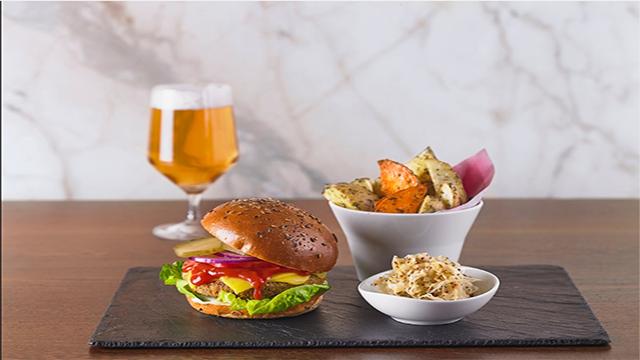 Vue sur une assiette d'ardoise comportant un burger végan, une portion de frites accompagnée d'une pinte de bierre.