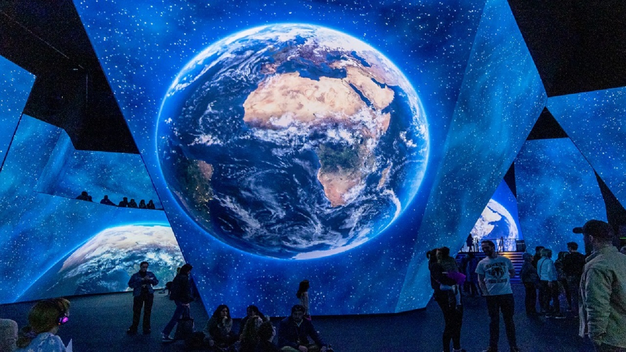 Regardez des images à couper le souffle des sept continents à la BBC Earth Experience. Avec l'aimable autorisation de BBC Earth Experience. grand espace d'exposition sombre avec des écrans numériques abstraits du sol au plafond, montrant des images de la Terre et de l'espace, et des personnes debout regardant les écrans.