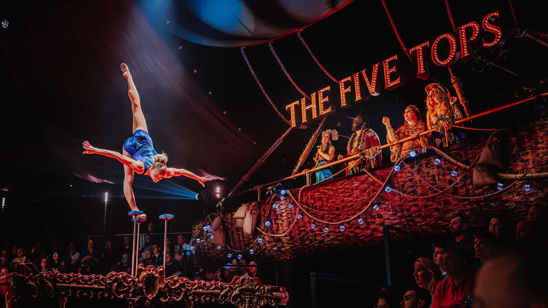 Watch circus acts, performances and jaw-dropping stunts at Come Alive! London: The Greatest Showman Circus London Spectacular. © London Theatre Direct/Luke Dyson circus tent with an audience watching an acrobat do the splits on an elevated stage in a spotlight