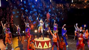 The cast of Come Alive! from The Greatest Showman stand at the centre of the Big Top, waving at the audience.