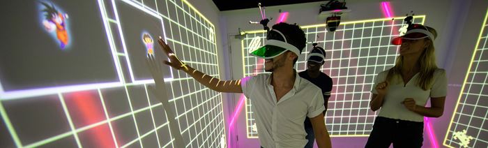 Eine Gruppe von Männern und Frauen, die in einem immersiven Spiel in einer mehrfarbigen LightBox in London neue Erfahrungen ausprobieren. 